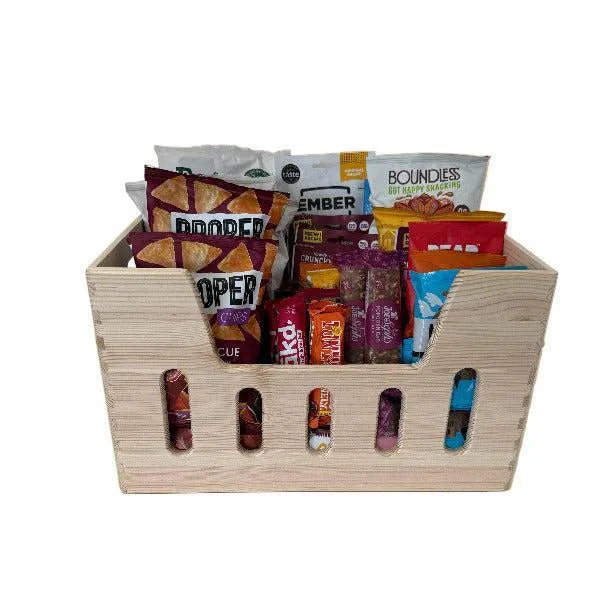 Wooden snack basket with a variety of snacks including chips and bars on a white background
