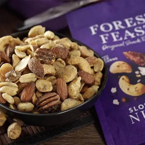 Forest Feast Slow roast nut mix in a bowl with a purple packaging of 'Forest Feast' nuts in the background.