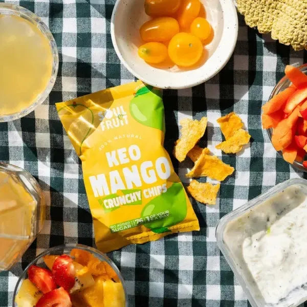 Soul Fruit Kéo Mango crunchy chips packaging on a checkered tablecloth with snacks and drinks.